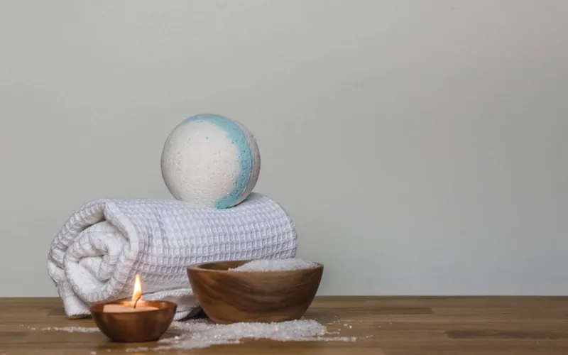 Toalla enrollada, cuenco con sales y una vela sobre una mesa de madera