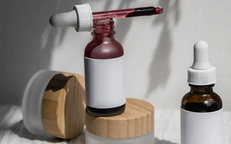 Frascos de sérum con gotario y envases de crema sobre un paño claro